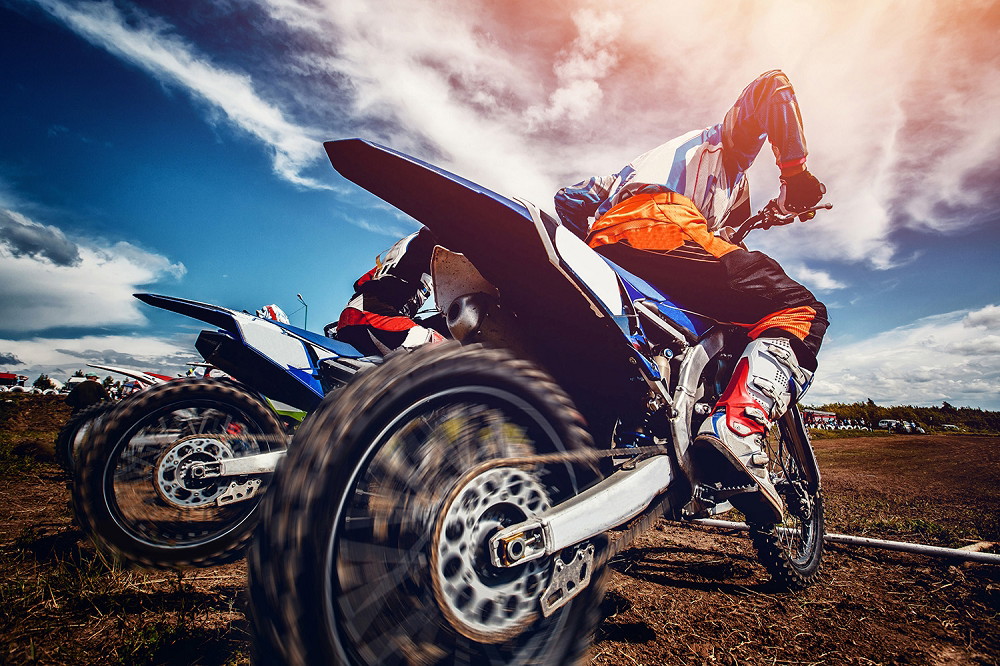 Wall mural - close-up of motocross bikes racing on an outdoor track, under a blue sky with clouds