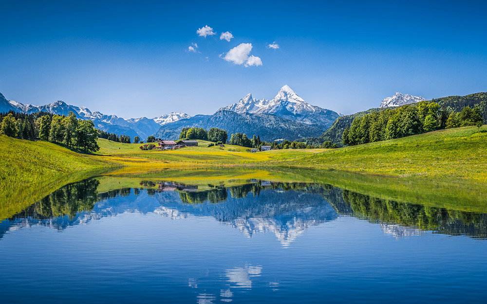 Fototapeta ścienna - Idylliczny alpejski krajobraz z wyraźnym odbiciem w wodzie, otoczony zielonymi łąkami i ośnieżonymi szczytami