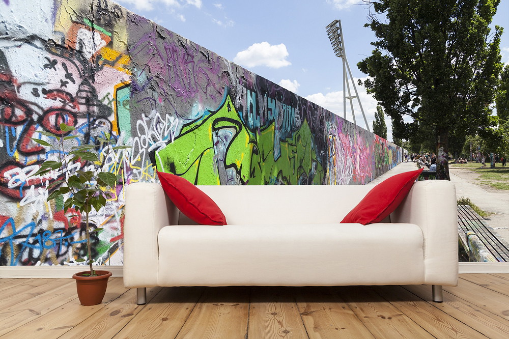 Papier peint photo - salon avec canapé blanc, coussins rouges et un mur avec des graffitis colorés, parc en arrière-plan