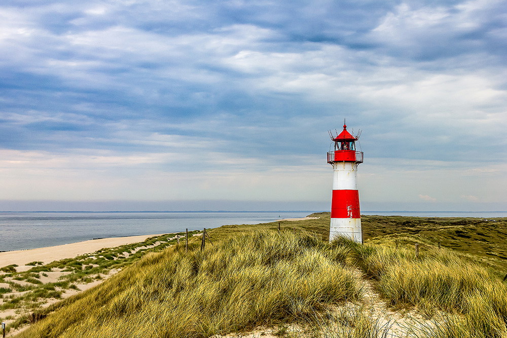 Fototapete - Leuchtturm in den Dünen an der Küste unter bewölktem Himmel