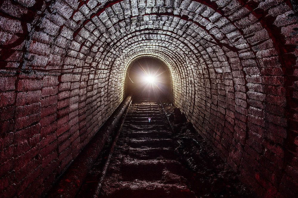 Wall mural - Brick tunnel with light visible at the end and a mystical atmosphere