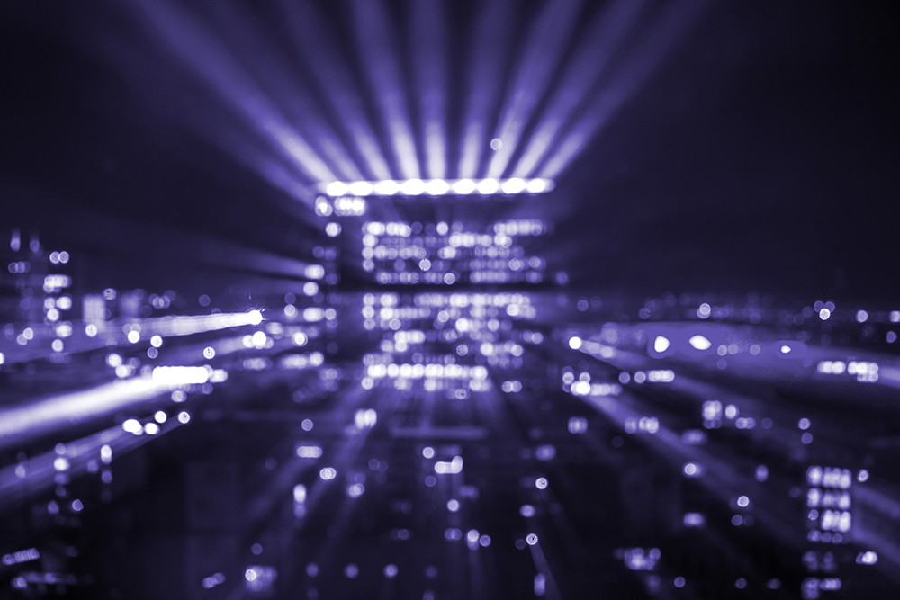 Muurschildering - Wazig uitzicht op een stad bij nacht, verlicht door lichtgevende lampen in paarse tinten