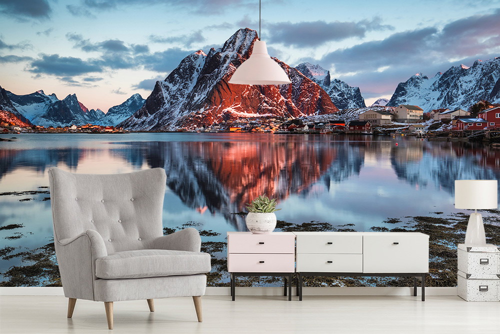 Fototapete - Ein ruhiger See spiegelnd schroffe Berge und einen klaren Himmel im Sonnenuntergang, im Hintergrund einer modern eingerichteten Wohnung.