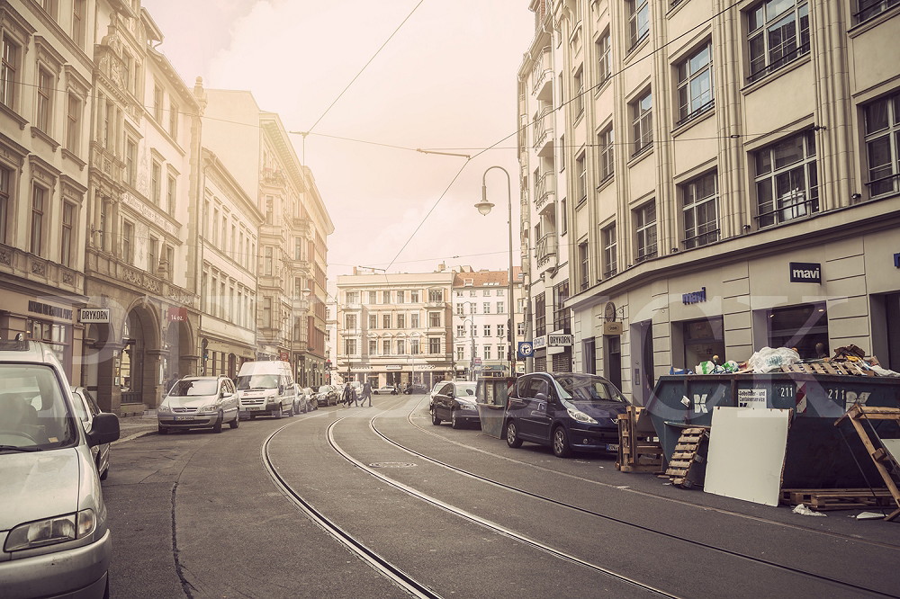 Papier peint photo - Rue historique avec des vieux bâtiments, des voitures garées et des rails de tramway vides au coucher du soleil