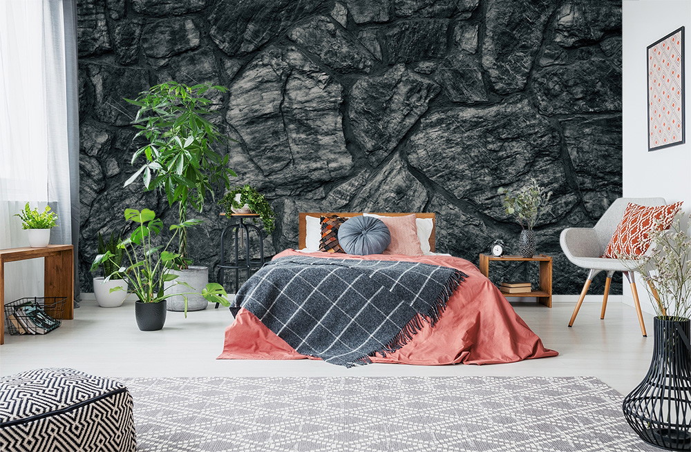 Papier peint photo - Chambre à coucher élégante avec un mur en pierre grise, un lit avec des coussins, des plantes en pot et un mobilier moderne.