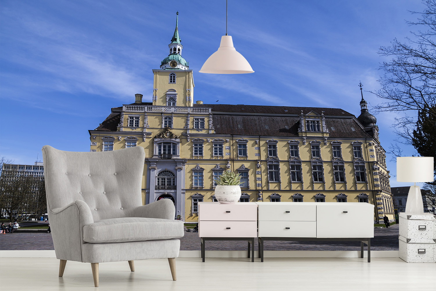 Papier peint photo - salon avec fauteuil gris et commode devant une image d'un bâtiment historique avec un ciel bleu