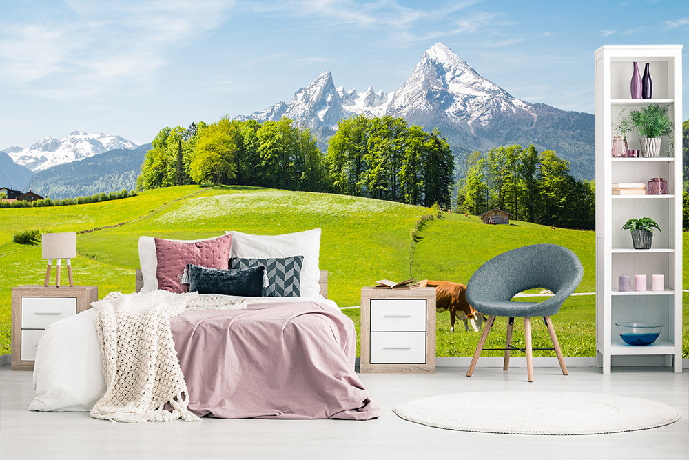 Fototapete - Schlafzimmer mit Fototapete von grünen Wiesen und schneebedeckten Bergen, eingerahmt von Bäumen.