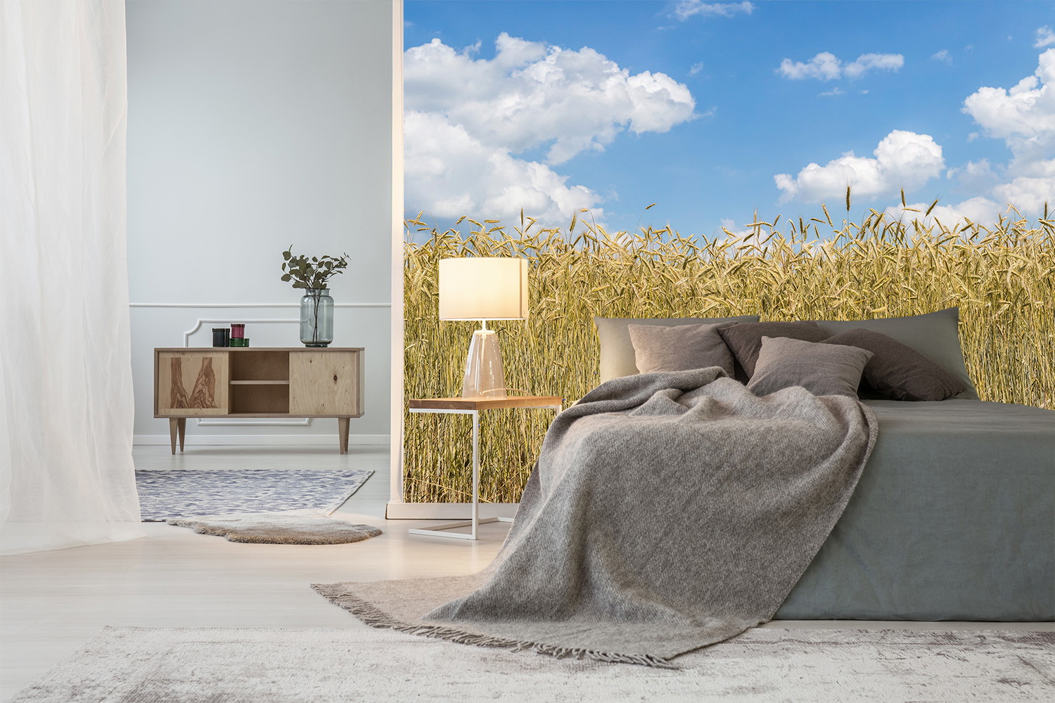 Papier peint photo - chambre avec un lit gris et un papier peint champêtre avec des champs de blé et un ciel bleu
