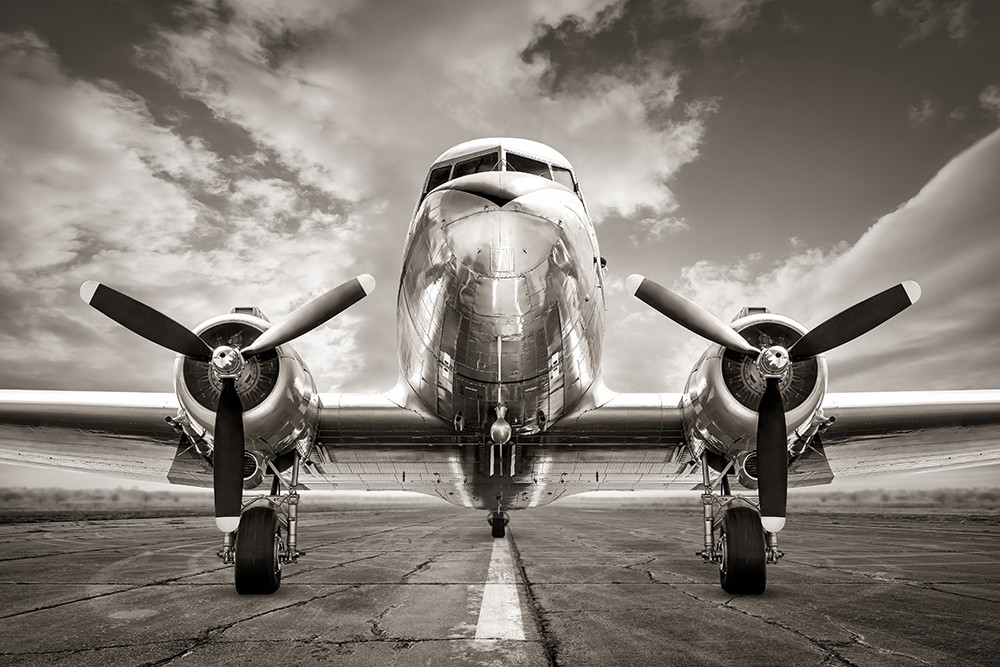 Fototapete - Frontansicht eines historischen Propellerflugzeugs in sepia, stehend auf einer Landebahn unter teilweise bewölktem Himmel
