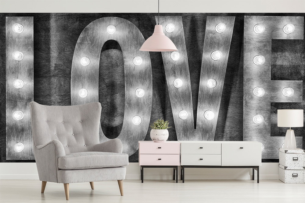 Fototapete - Wohnzimmer mit großem LOVE-Schriftzug aus Metall und Lichtern, grauem Sessel und minimalistischen Möbeln
