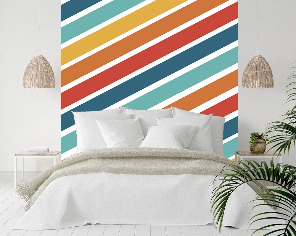 Fototapete - Schlafzimmer mit bunter diagonaler Streifenmuster-Wand hinter einem weißen Bett, dekoriert mit Pflanzen und Hängelampen.