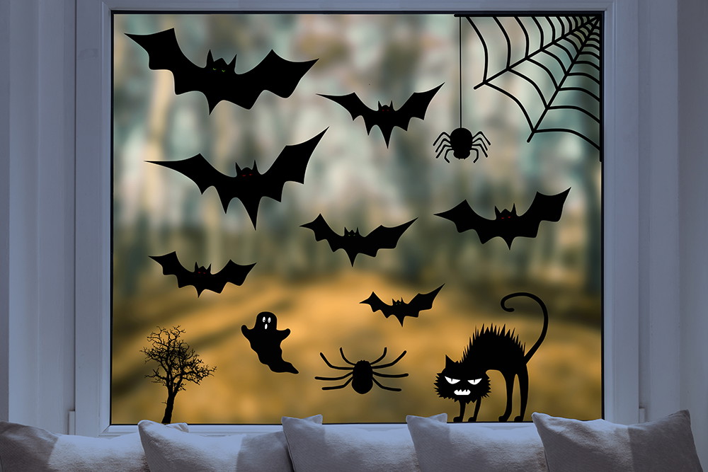Fenstersticker - Fensterdekoration mit Halloween-Thema, inklusive Fledermäusen, Spinne im Netz, schwarzer Katze und Gespenst vor unscharfem Hintergrund