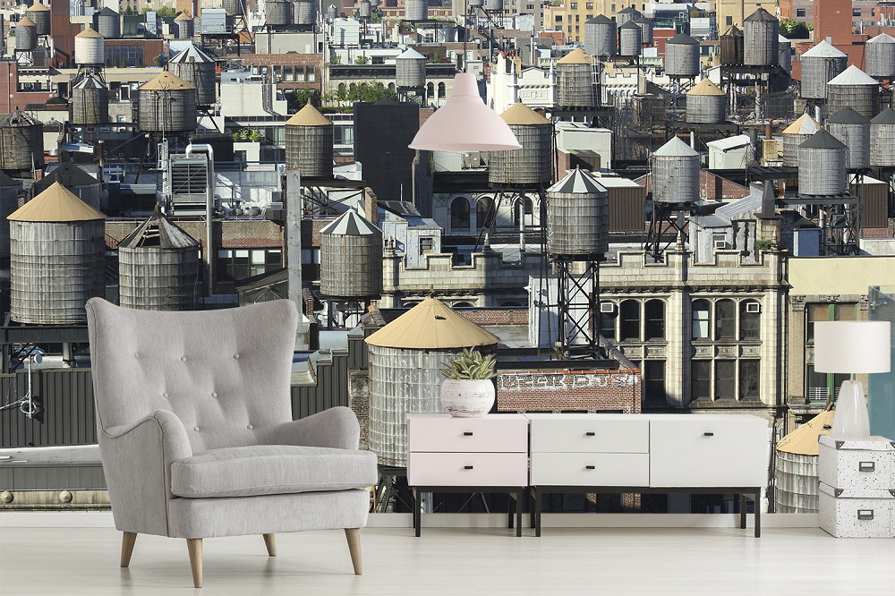 Wall mural - living room with urban wall mural of city view and water tanks, grey armchair and mid-century chest of drawers
