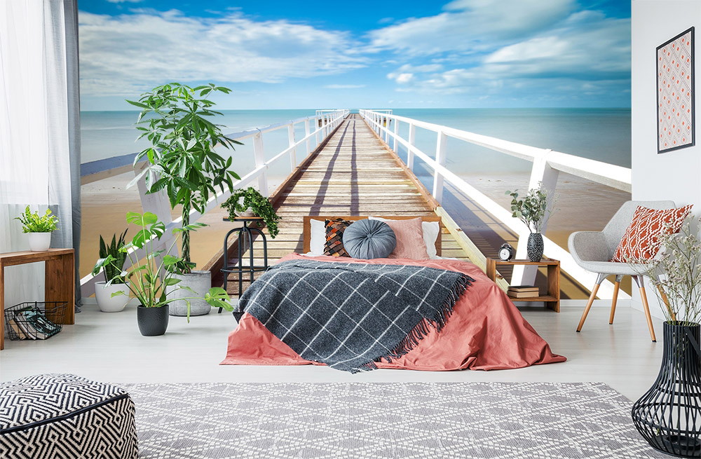 Fototapete - Schlafzimmer mit großformatiger Steg-und-Meer-Tapete, umgeben von Pflanzen und stilvollen Möbeln