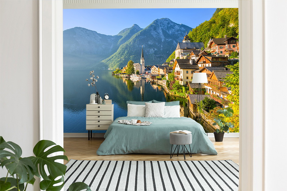 Papier peint photo - Chambre à coucher avec papier peint représentant Hallstatt au bord du lac et les montagnes, avec un lit confortable et des plantes au premier plan