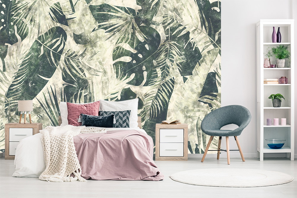 Fototapete - Zimmer mit tropischem Blättermotiv, Bett mit rosa Decke und Kissen, grauer Stuhl und Regal