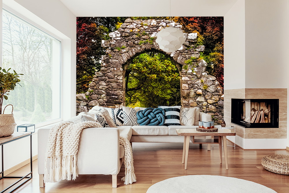 Papier peint photo - Arche de pierre antique avec vue sur un jardin verdoyant derrière un canapé moderne dans le salon