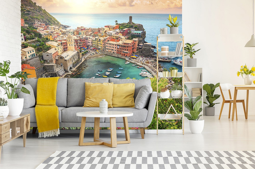 Fotobehang - Woonkamer met grijze bank en gele deken, met een afbeelding van een kleurrijk kuststadje met uitzicht op zee
