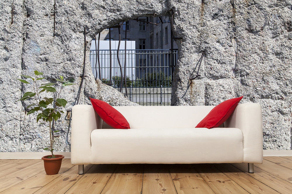 Fototapeta - Jasna sofa z czerwonymi poduszkami przed tapetą ze ścianą i widokiem przez otwór