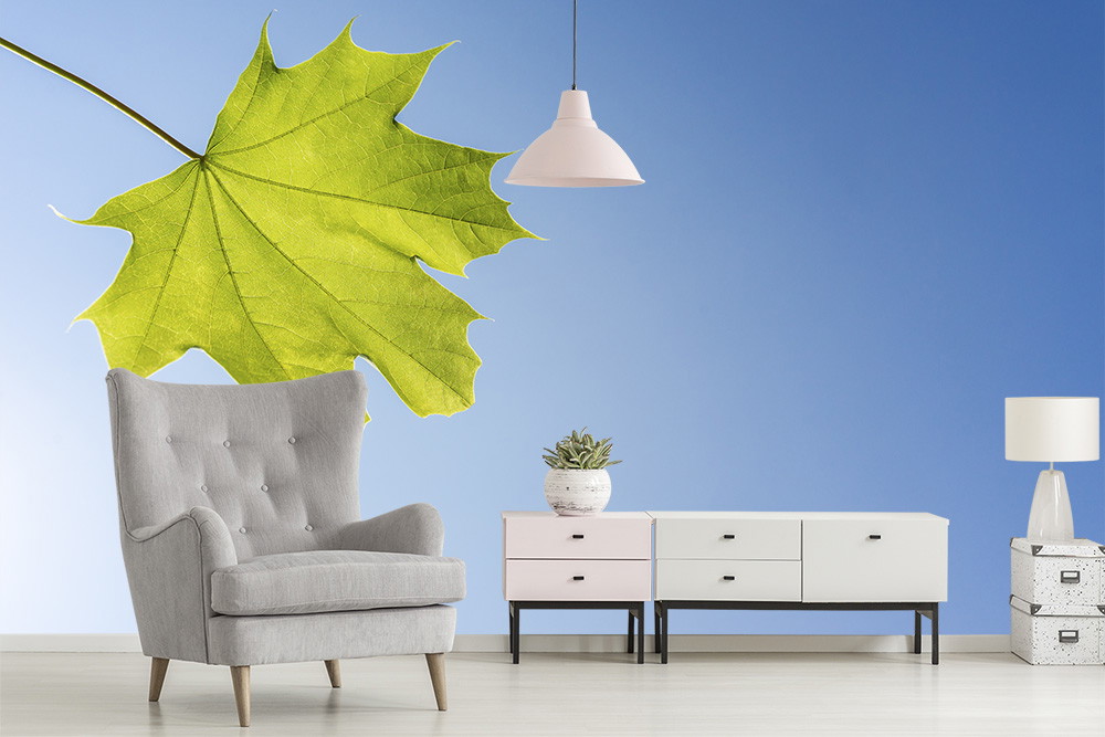 Fototapete - Stilvolles Wohnzimmer mit grauem Sessel, Kommode, Lampe und grüner Blatttapete vor blauer Wand