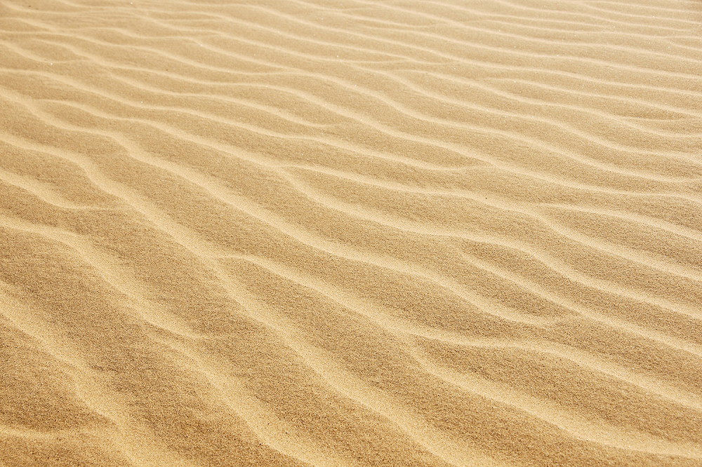 Fototapete - Nahaufnahme eines wellenförmigen Sanddünenmusters in der Wüste, von Sonnenlicht beschienen