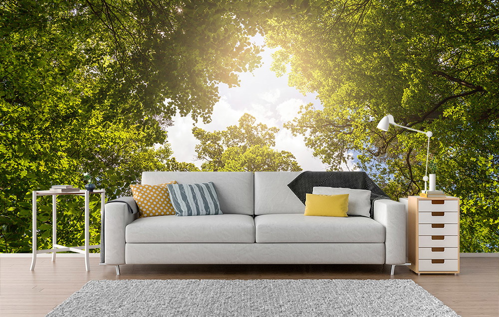 Fototapete - Wohnzimmer mit weißem Sofa und Waldblick als Hintergrund, umgeben von grünen Baumkronen und natürlichem Licht