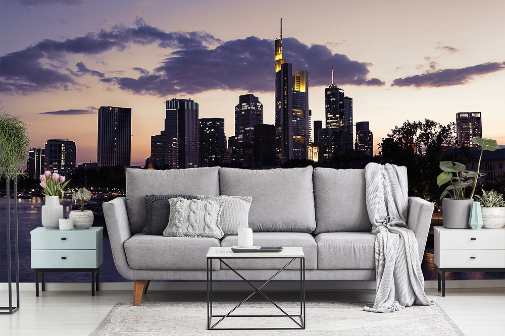Fototapeta - Szara sofa przed tapetą z panoramą miasta o zachodzie słońca, otoczona roślinami i stolikami bocznymi w nowoczesnym salonie