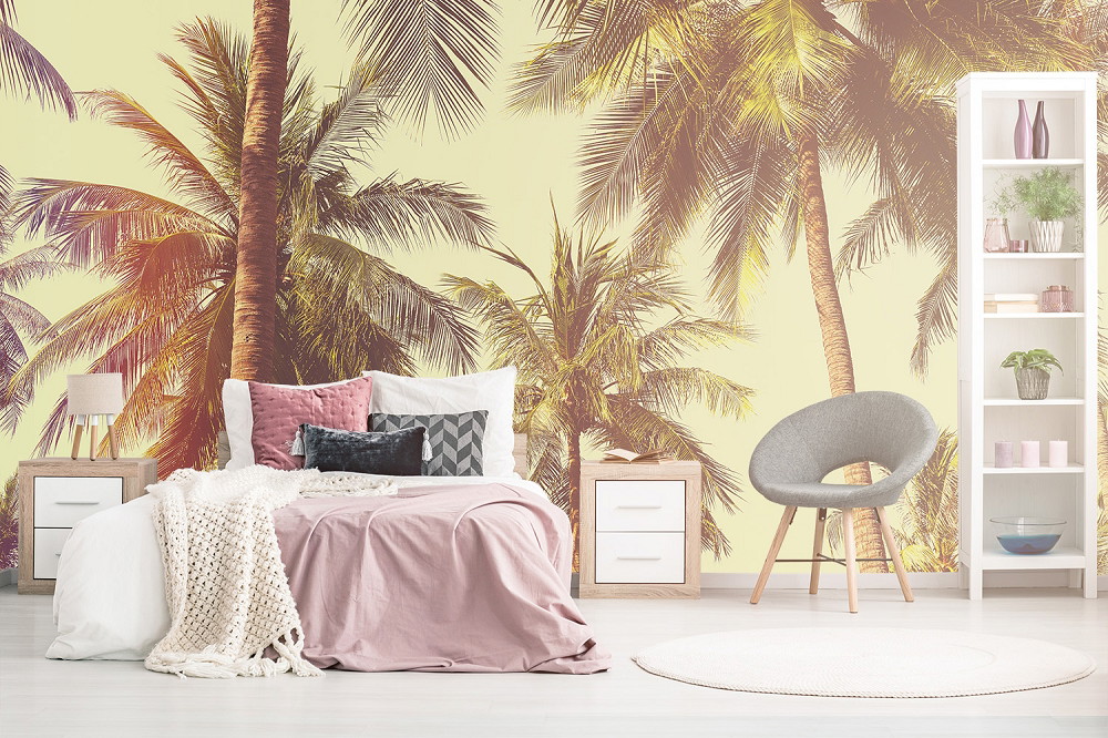 Fototapete - Modernes Schlafzimmer mit Fototapete von Palmen, Bett mit rosa und grauen Kissen, weißen Nachttischen, grauem Stuhl und dekorativem Regal