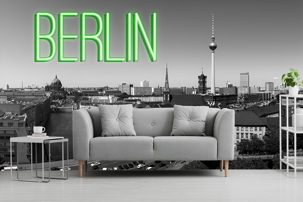 Fototapete - Panoramablick auf Berlin mit grün leuchtendem BERLIN-Schriftzug und grauem Sofa im Vordergrund