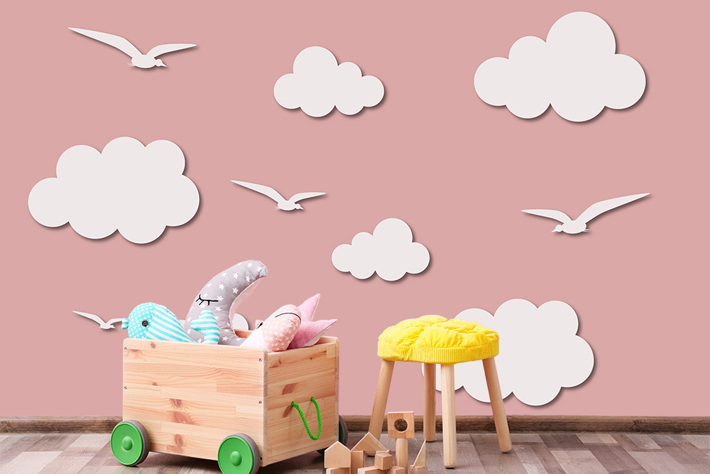 Fototapete - Rosa Kinderzimmerwand mit weißen Wolken und Möwen, Holzspielzeug und Sitzhocker