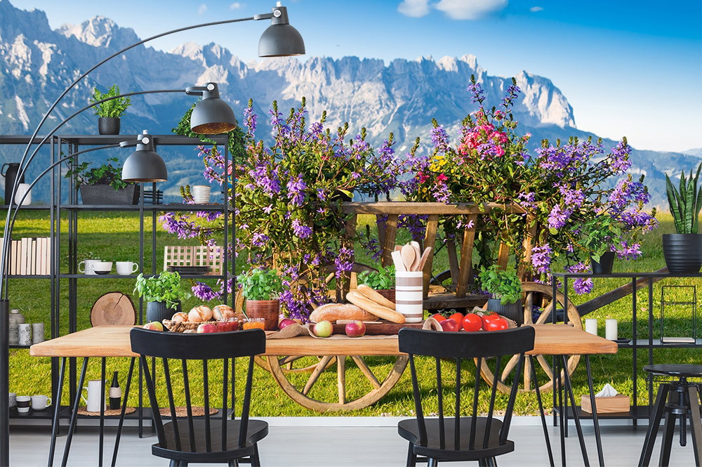 Fototapete - Ein Esszimmer mit einem Tisch voller Lebensmittel, einem Blumenwagen und einem Bergpanorama im Hintergrund