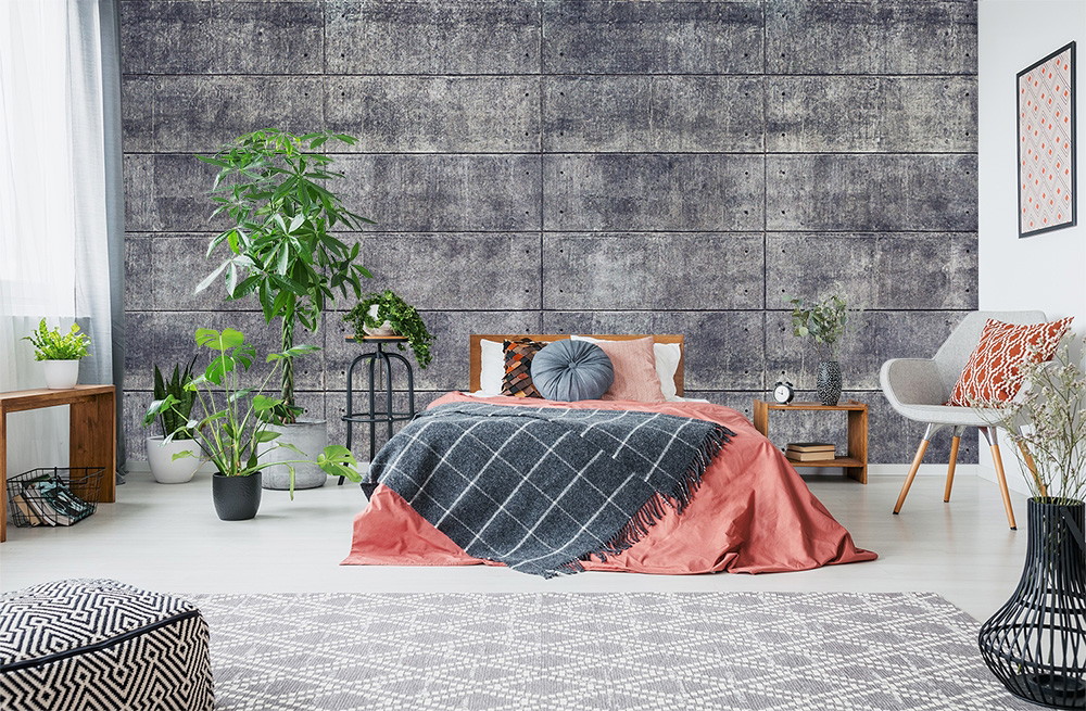Fototapete - Schlafzimmer mit Betonwand, Pflanzen, Bett mit rosa Decke und grauen Kissen