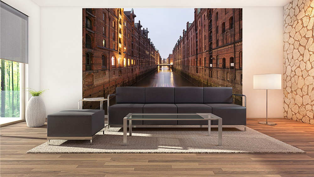 Wall mural - living room with sofa and glass coffee table, background shows the warehouse district in the evening with illuminated buildings