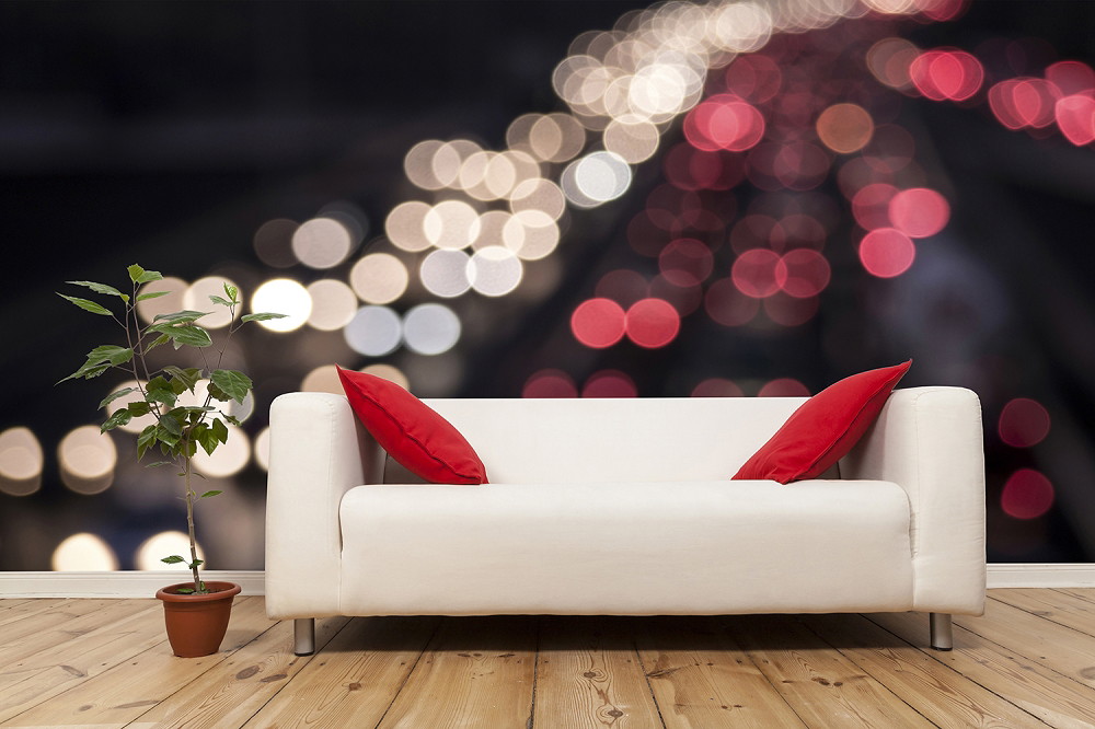 Fototapeta - Biała sofa z czerwonymi poduszkami na rozmytym tle świateł miasta, obok rośliny doniczkowej na drewnianej podłodze