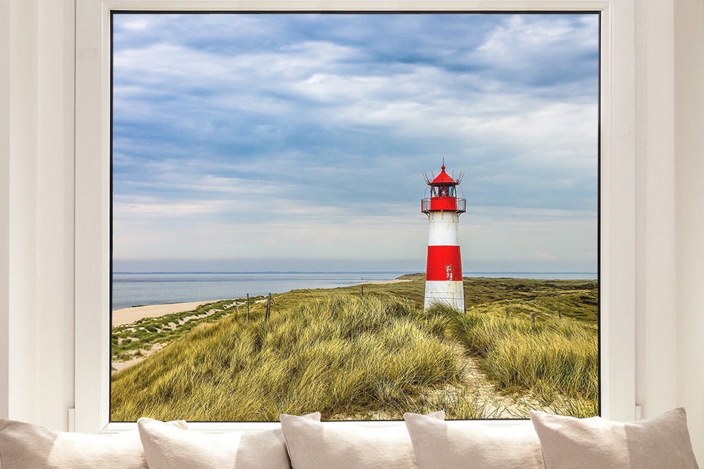 Fensterfolie - Fensterblick auf einen rot-weißen Leuchtturm umgeben von Dünen am Meer unter wolkigem Himmel