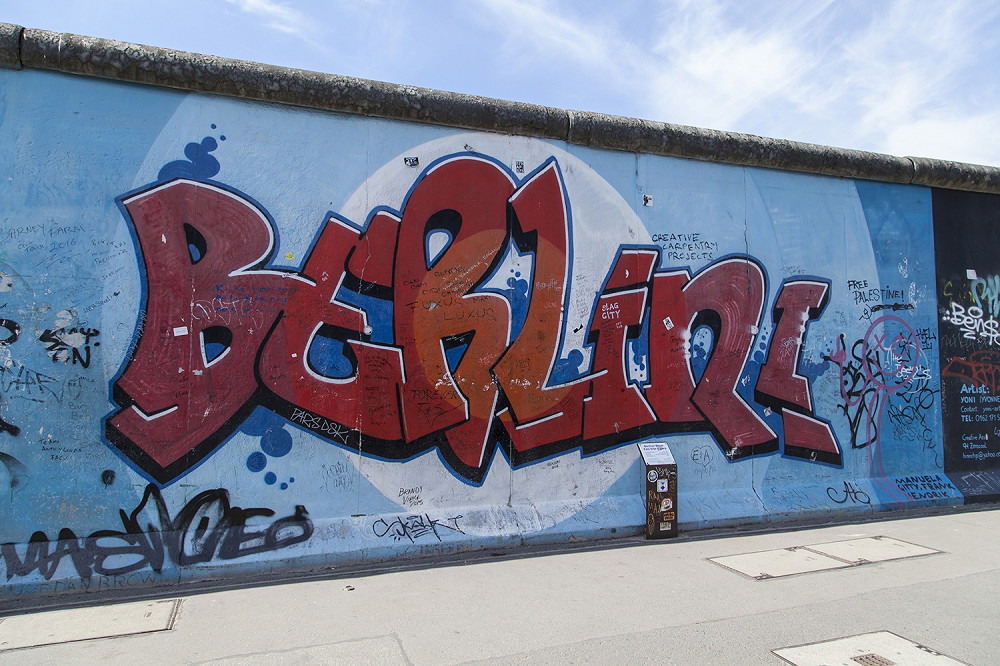 Muurschildering - Graffiti 'Berlijn' op de Berlijnse Muur, omringd door blauwe muur en lucht