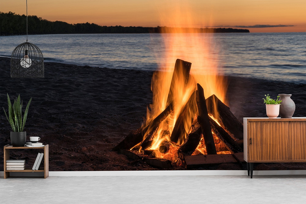 Muurschildering - Kampvuur op het strand bij zonsondergang met warme vlammen voor de kalme zee