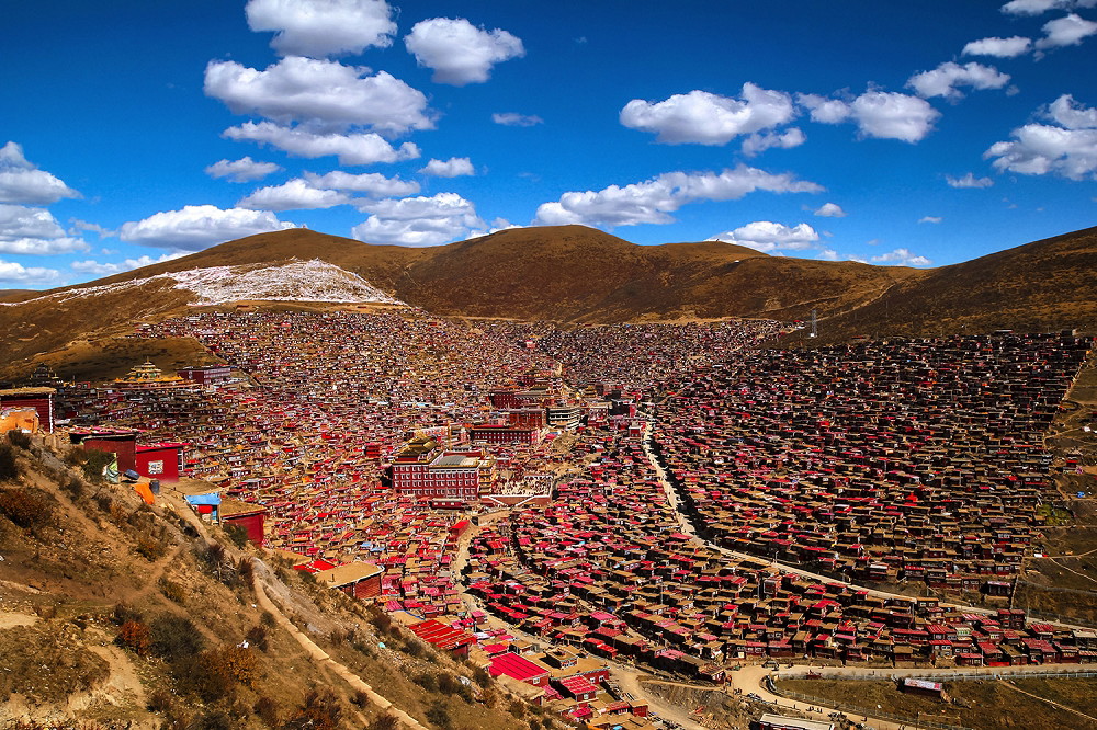 Fototapete - Weitläufige buddhistische Siedlung in bergiger Umgebung mit zahlreichen roten Dächern und klarem, blauem Himmel