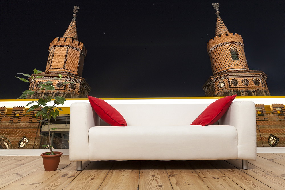 Fototapeta - Biała sofa z czerwonymi poduszkami przed ścianą z fototapetą wież mostu berlińskiego nocą