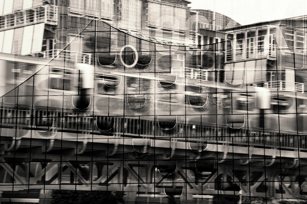 Wall mural - black and white photograph of an urban scene with reflection showing buildings and a passing railway