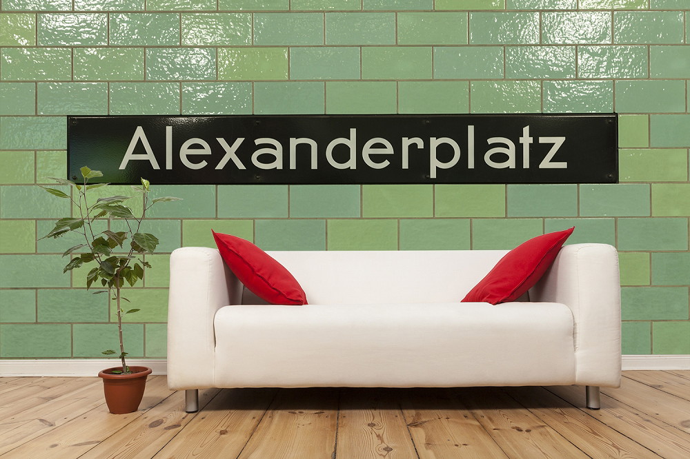 Fototapete - Stilvolles Wohnzimmer mit Sofa, roten Kissen und Alexanderplatz-Tafel an der Wand