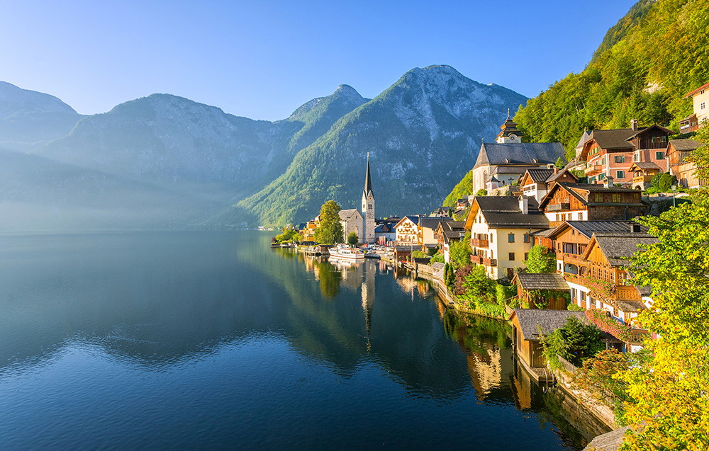 Fototapeta ścienna - Idylliczna wioska Hallstatt z tradycyjnymi domami, spiczastą wieżą kościoła i spokojnym jeziorem otoczonym majestatycznymi górami