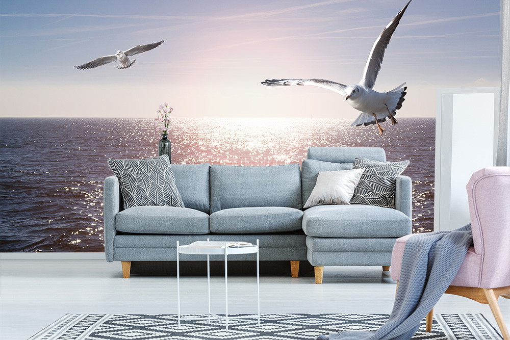 Fototapete - Wohnzimmer mit Sofa und Möwen über einem glitzernden Meer bei Sonnenuntergang