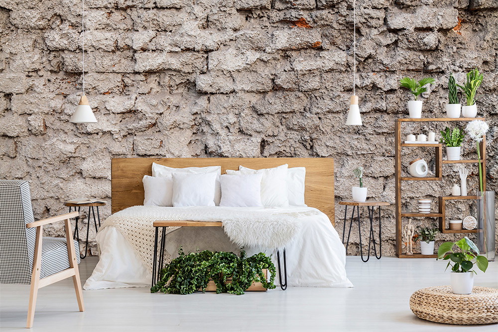 Papier peint photo - chambre à coucher avec mur en pierre rustique, lit moderne, plantes et meubles minimalistes