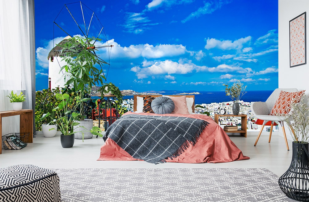 Fototapete - Ein Schlafzimmer mit mediterranem Flair, Pflanzen, Blick auf das Meer und eine traditionelle Windmühle im Hintergrund.
