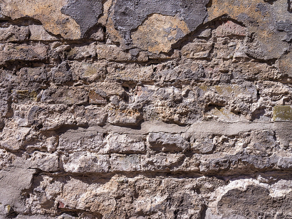 Wall mural - Close-up of an old stone wall with rough texture and different layers of colour