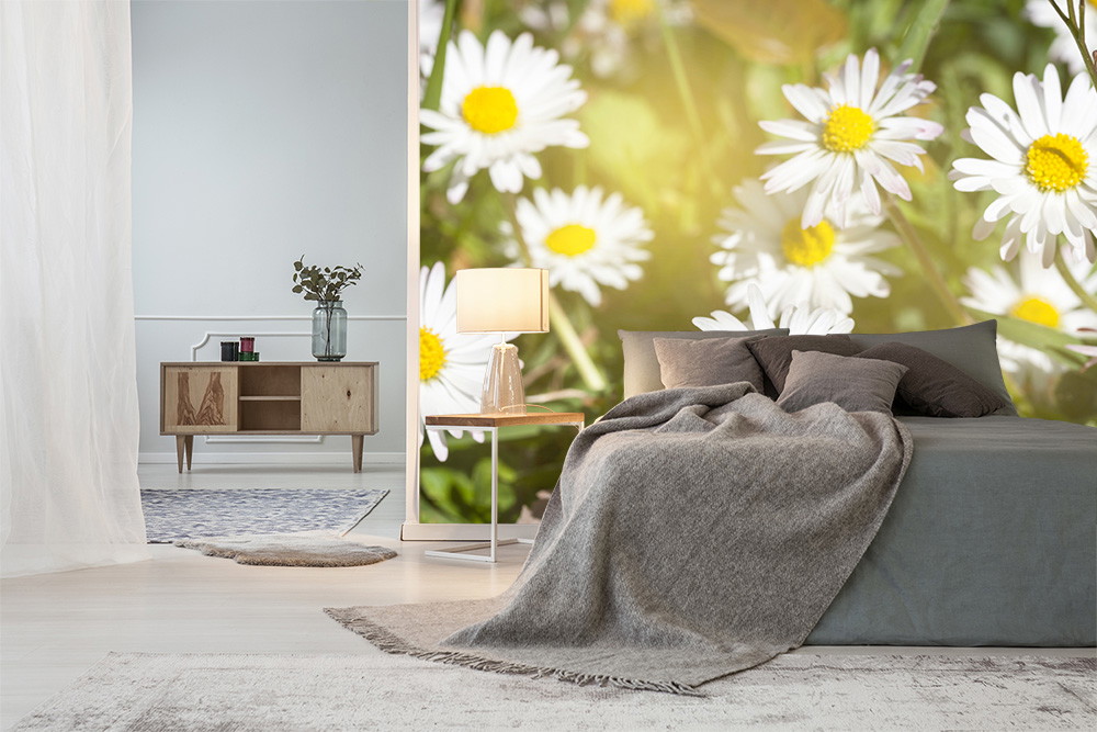 Fototapete - Schlafzimmer mit Gänseblümchen-Fototapete, grauem Bett, Holzkommode und Lampe