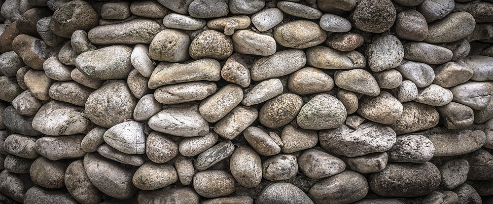 Wall mural - Detailed view of a wall of natural river pebbles arranged in different shades of grey