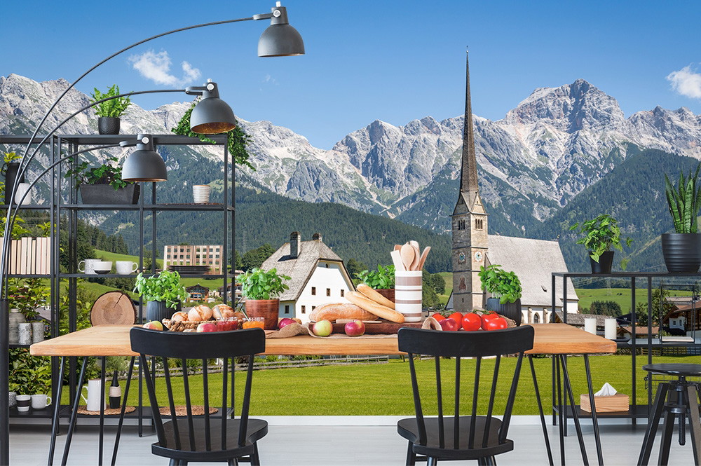Fototapete - Moderner Essbereich vor einer malerischen Landschaft mit Kirche und Alpen im Hintergrund