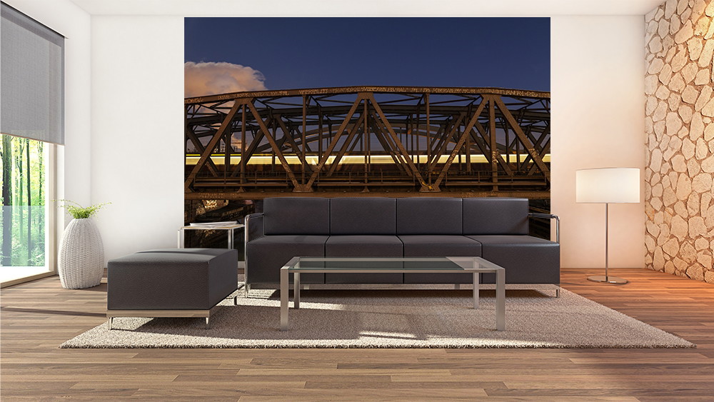 Fototapete - Stilvolles Wohnzimmer mit dunkler Couch und Glas-Couchtisch, das eine Fototapete mit einer beleuchteten Brücke bei Nacht zeigt.
